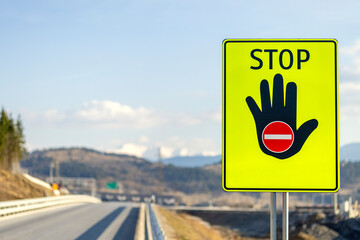 Yellow reflective stop sign on the side of the highway. Raised hand to stop with red traffic sign no entry