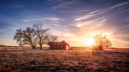 Naklejka premium Old abandoned wooden farmhouse on the prairie at sunset. Colorful clouds float silently in the sky. 