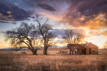 Old abandoned wooden farmhouse on the prairie at sunset. Colorful clouds float silently in the sky. 