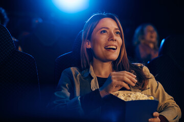 Happy woman eating popcorn during film screening in theater.