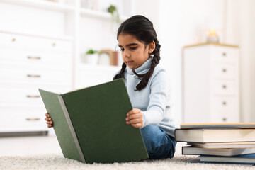 Naklejka premium Cute little girl reading book on floor at home
