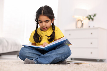 Naklejka premium Cute little girl reading book on floor at home