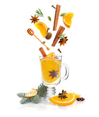 Mulled wine recipe. Spices and other ingredients falling into glass cup with beverage against white...