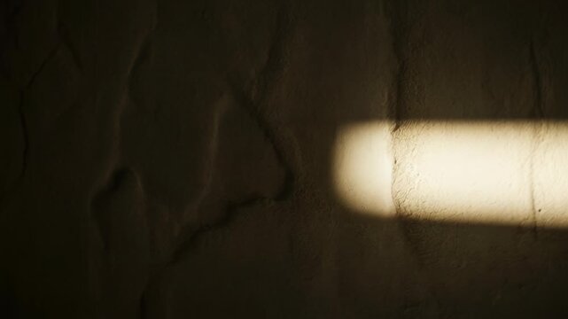 Soft light filters through a window and casts a warm rectangle on a textured wall, creating an abstract interior scene.