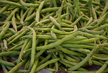 Fresh green beans piled together creating a natural vegetable background. Close-up view of raw organic string beans commonly sold at farmers markets and grocery stores. Healthy plant-based food.