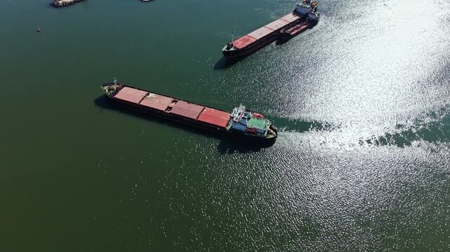 Two cargo ships move through the water. The sun reflects on the surface. They are in a busy area where shipping is common.
