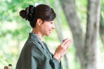 Obraz premium A young Asian woman wearing a yukata haori relaxing on the veranda of a guest room in a ryokan (Japanese inn) while drinking sake