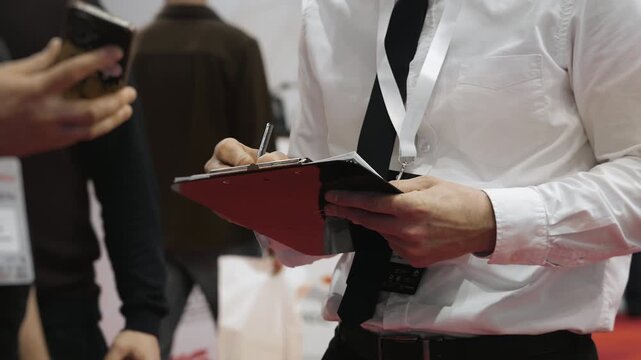 Event staff checking attendee information and writing on clipboard during conference registration at corporate business event.