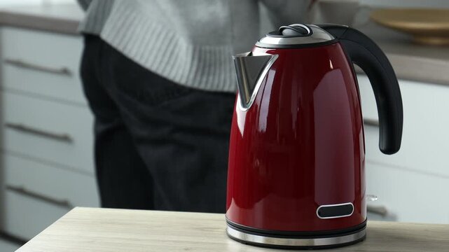 Woman pouring hot water from electric kettle into cup at wooden table indoors, closeup