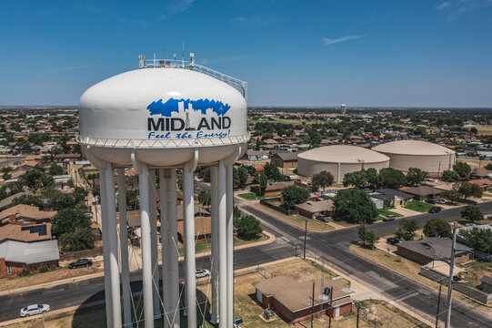 Aerial Drone View of Tall White Water Tower Surrounded By Buildings and Streets With Blue Sky in Downtown Midland, Texas