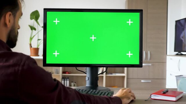 Man Typing on Computer With Green Screen Mockup in Home Living Room