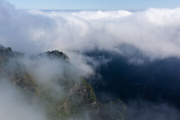 Fototapeta premium Cliffs at Curral das Freiras shrouded in mist. Dense fog blankets the lush green mountains. The serene landscape of Madeira Island, Portugal. A tranquil scene above the clouds.