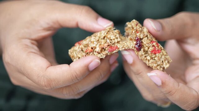 Woman hands breaking healthy granola bar with dried fruits and nuts in slow motion close up, delicious homemade snack, nutritious vegan food