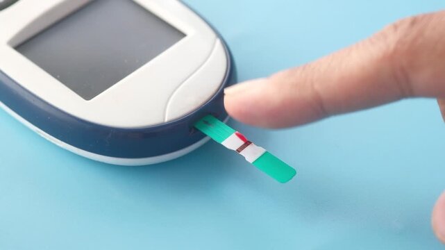 Close up of glucose meter test strip receiving blood drop for diabetes test
