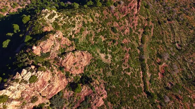 Aerial perspective shows rocky hills covered with green plants under clear skies. The landscape features rugged terrain and patches of vegetation.