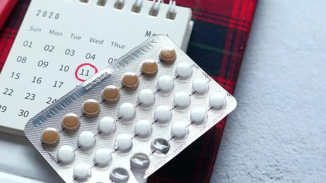 Birth control pill strip on calendar background with red date circle marking menstrual cycle and contraception management