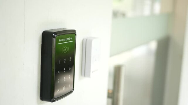Digital access control keypad mounted on wall near office glass door for security authentication