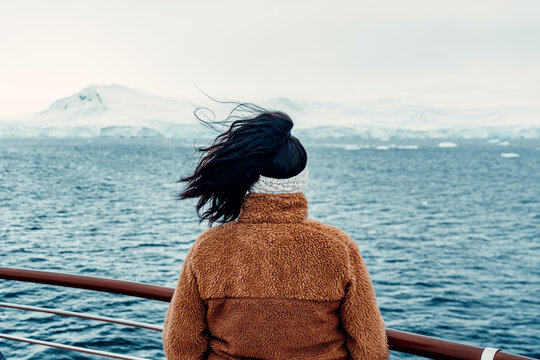 Woman looks over the water towards snowy mountains in Antarctica during a travel tour on a ship in the afternoon