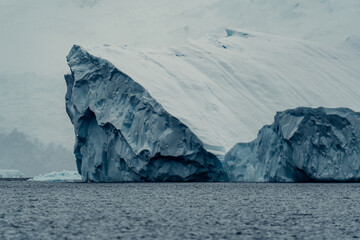 Large icebergs float in the freezing waters of Antarctica near the shoreline under a cloudy sky © ANITEK MEDIA 