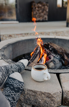 A woman sitting by a fire with a cup of coffee .