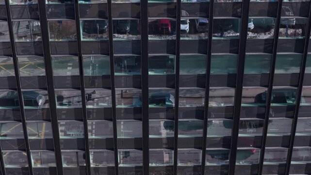 Drone view of a modern office building glass facade reflecting parked cars, street lines, and urban surroundings. Architectural pattern and reflective windows in Vilnius, Lithuania.