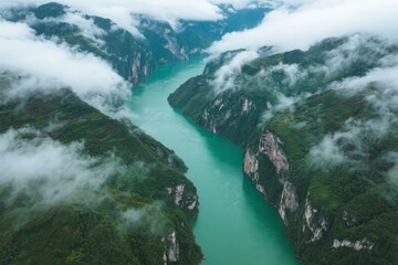 Fototapeta premium Aerial view of a turquoise river winding through mist-covered mountain valleys