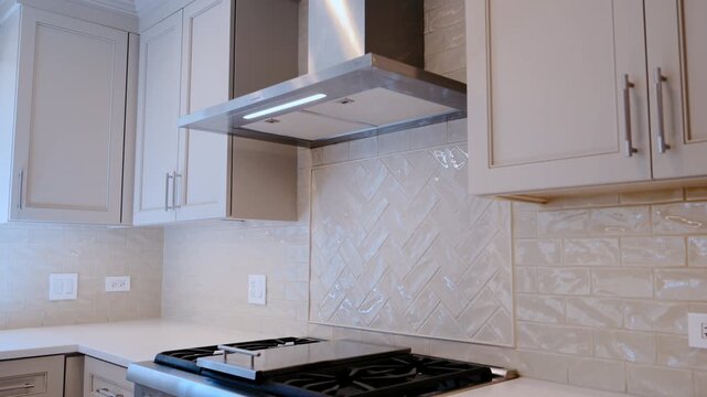 Modern kitchen interior with stainless steel range hood, white cabinets, and tiled backsplash. Clean contemporary residential design detail.