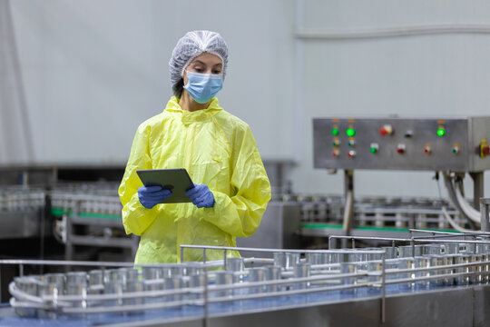 Clean room technician using tablet to inspect an automated production line in Canned food factory factory, highlighting quality control, hygiene standards, industrial safety, smart manufacturing.