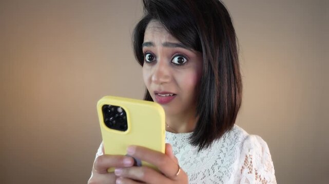 Close up of shocked surprised young Asian cute girl woman hold phone receive shocking news looking at camera with astonished stunned face expression, isolated over grey studio background.