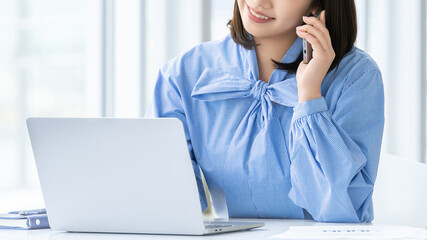 パソコンを見ながらスマートフォンで通話する女性ビジネスパーソン, Businesswoman talking on smartphone while looking at laptop © Trickster*