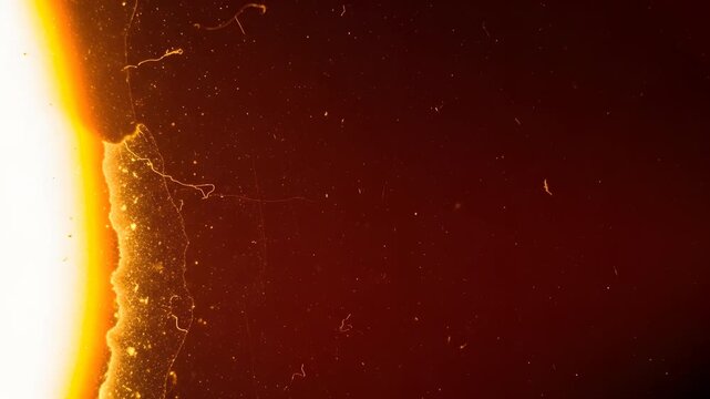A striking film burn overlay transition alternates between pitch-black frames and a vivid, fiery orange crack that sears diagonally across the visual field, complete with glowing embers and scratches