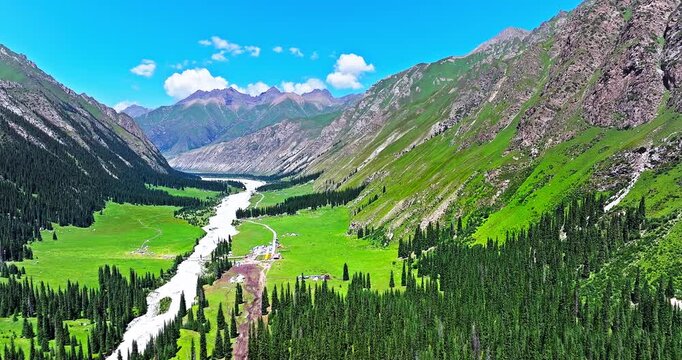 Breathtaking aerial view of a lush green valley with a meandering river and dense forest in the Tianshan Mountains, Xinjiang, China.