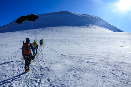 Mountaineers in rope team with crampons ascending towards mountain summit Parrotspitze and glacier panorama in the morning in Pennine Alps, Italy