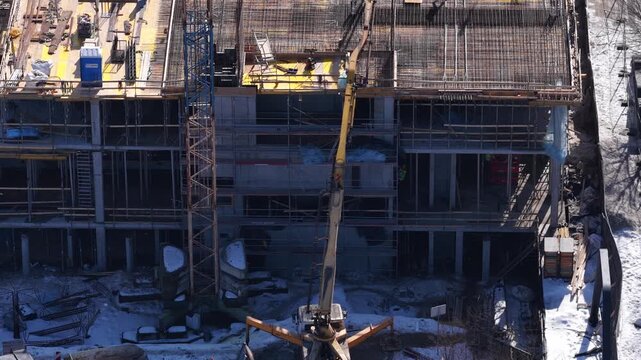 Aerial drone view of an active construction site with tower crane, reinforced concrete framework, workers, and building structure under development during winter in Vilnius, Lithuania.