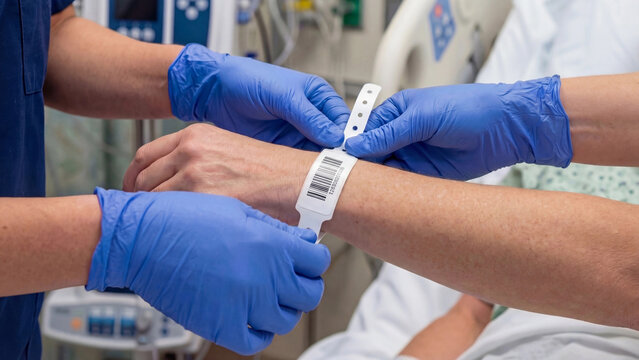 Nurse attaching barcode identification wristband to hospital patient wrist for medical record tracking patient safety clinical admissions and healthcare identity verification procedure