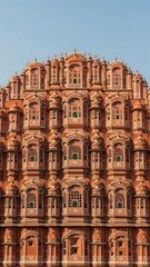 Fototapeta premium Intricate sandstone facade of Hawa Mahal palace with numerous latticed windows and ornate balconies, showcasing detailed Rajasthani architecture against a clear blue sky.