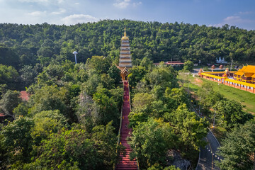 Obraz premium Aerial view of naga staircase leading through lush forest to pagoda tower at Wat Benjakhirinakhon under blue sky in Ratchaburi, Thailand