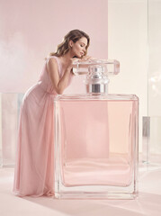 Woman in pink dress leaning on oversized perfume bottle in elegant setting  