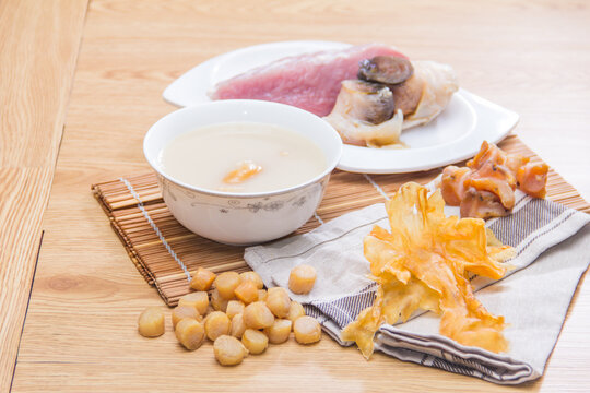 A white porcelain bowl of creamy congee served with dried scallops, pork slices, and mushrooms on a wooden mat.