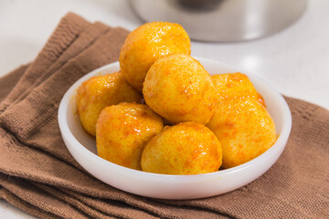 A white bowl filled with golden fish balls coated in shiny sweet glaze, placed on a brown cloth.