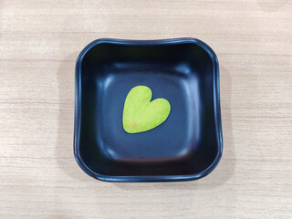 Green Heart Shaped Wasabi Paste in a Black Bowl on Wooden Table Surface Top View