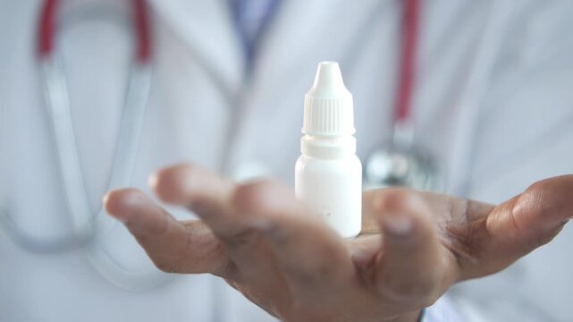 Doctor holds eye drop bottle in hand, medical concept with stethoscope background