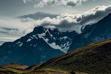 Fototapeta premium Mountains in Patagonia under cloudy skies during an afternoon hike with snow on the peaks and shadow on the hills