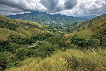 Obraz premium Rolling green hills frame a distant valley town, under dramatic cloudy skies
