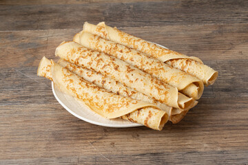 Stack of thin crepes on a white plate placed on a wooden table