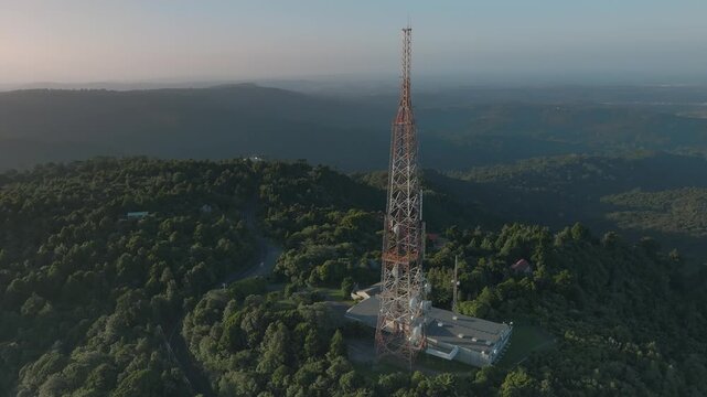Aerial view of a tall telecommunications tower on a forested hilltop in Auckland, New Zealand. The tower provides essential communication services to the region.