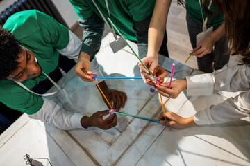 Overhead view of hands in green sleeves building a structure from recycled plastic straws.