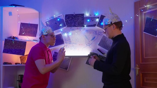 Two Caucasian Men Planning Alien Search At Whiteboard, Collaborative Stance With Foil Hats, Exchanging Notes And Diagrams Under LED Lights, Strategic Discussion And Investigative Preparation