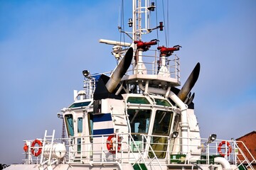 Close up of a white tugboat bridge with exhaust stacks and fire monitors. Industrial maritime vessel detail for shipping, nautical, and harbor maintenance design under a clear sky. © Igor