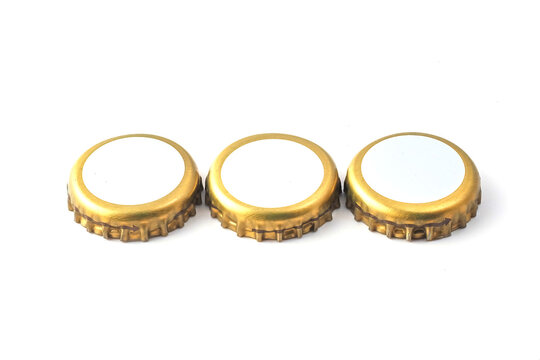  Three golden metal beer bottle caps with white blank tops isolated on white background. Minimalist mockup for beverage branding, brewery logo presentation and craft soda packaging design.